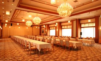 a large , well - lit banquet hall with rows of tables and chairs arranged for a formal event at Zazan Minakami