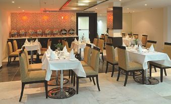 a restaurant with multiple dining tables and chairs , each set with white tablecloths and napkins at Amara Hotel