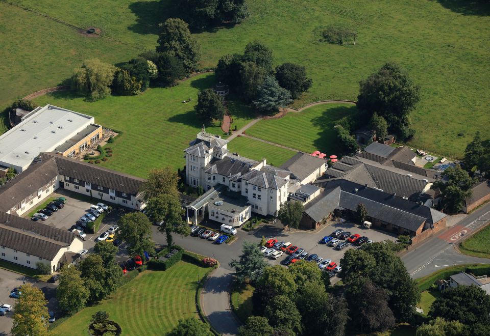 an aerial view of a large building surrounded by grass and trees , with several cars parked in the lot at Thornton Hall Hotel & Spa