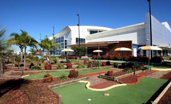 a miniature golf course with a building in the background , surrounded by palm trees and umbrellas at Mercure Sydney Liverpool