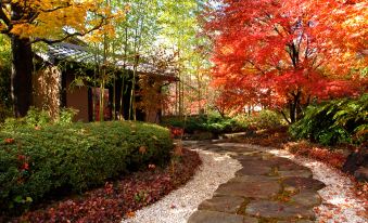 a beautiful garden with a stone pathway , trees in various colors , and a house with a chimney at Miyako