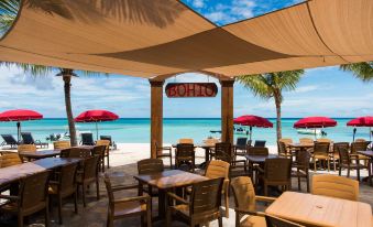 a beachside restaurant with wooden tables and chairs , umbrellas , and palm trees under a canopy at Bohio Dive Resort