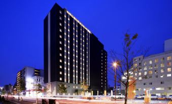 a tall hotel building surrounded by trees and a street at night , illuminated by street lights at Hotel Monte Hermana Fukuoka