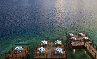 a wooden pier extending into the ocean , with several tables and chairs set up for dining at Coco Bodu Hithi