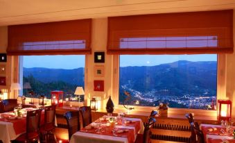 a restaurant with large windows offering a view of the city and mountains , featuring a dining table set for a meal at Hôtel Panorama