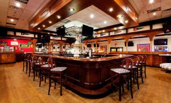 a bar with a wooden ceiling , surrounded by chairs and tables , and a television mounted on the wall at Holiday Inn Long Island - Islip Arpt East