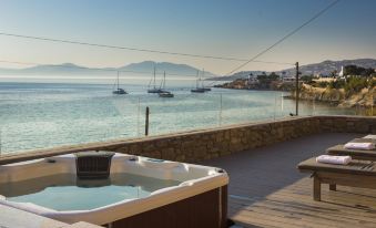 a hot tub is seen in the foreground , with a view of boats and mountains in the background at Mykonos Beach Hotel