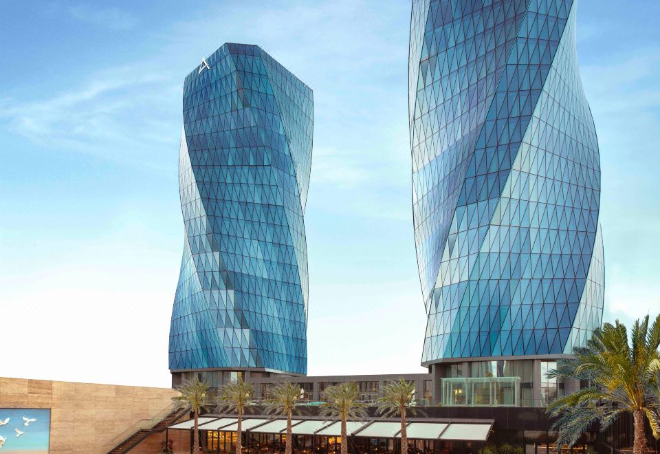 two tall , blue buildings with glass roofs are next to a swimming pool and palm trees at Burgu Arjaan by Rotana