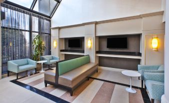 a modern living room with large windows , a green bench , and two televisions on the wall at Holiday Inn Washington-Dulles International Airport, an IHG Hotel