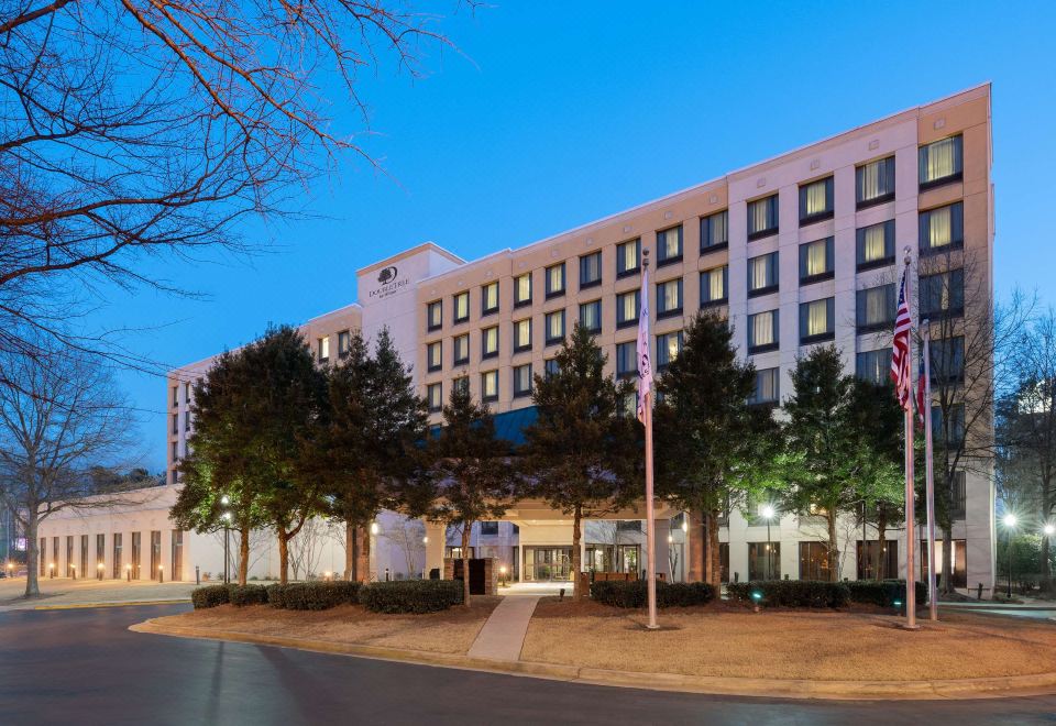a large hotel building with multiple stories , surrounded by trees and lit up at night at DoubleTree by Hilton Atlanta Airport