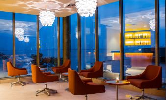 a modern living room with large windows , orange chairs , and circular lights hanging from the ceiling at Radisson Blu M'Bamou Palace Hotel, Brazzaville