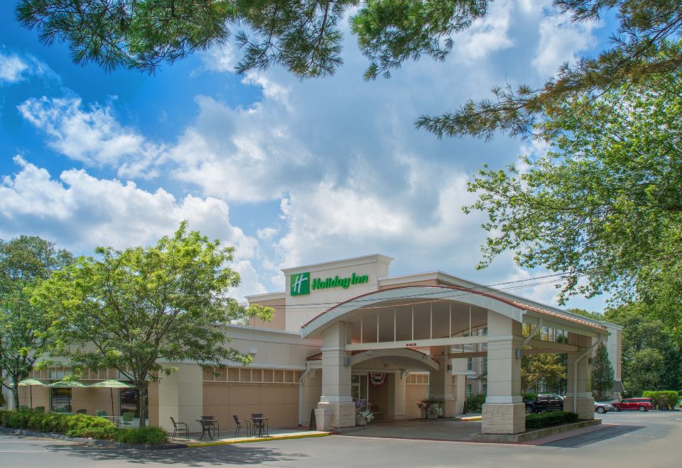 a holiday inn express hotel with its entrance and parking lot , under a blue sky dotted with clouds at Holiday Inn South Kingstown (Newport Area)