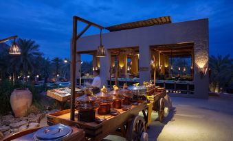 a large outdoor dining area with a buffet table filled with various food items , including fruits and desserts at Six Senses Zighy Bay
