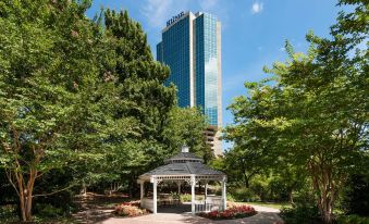 a city park with a gazebo surrounded by lush green trees and tall buildings in the background at Hilton Alexandria Mark Center