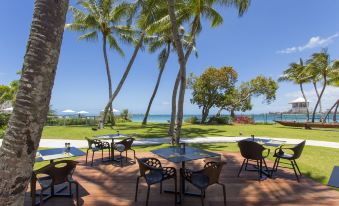 a patio area with several tables and chairs , surrounded by palm trees and a view of the ocean at Chateau Royal Beach Resort & Spa, Noumea