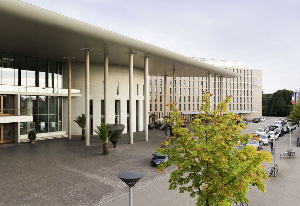 a modern building with a large courtyard in front of it , surrounded by trees and benches at Novotel Freiburg am Konzerthaus