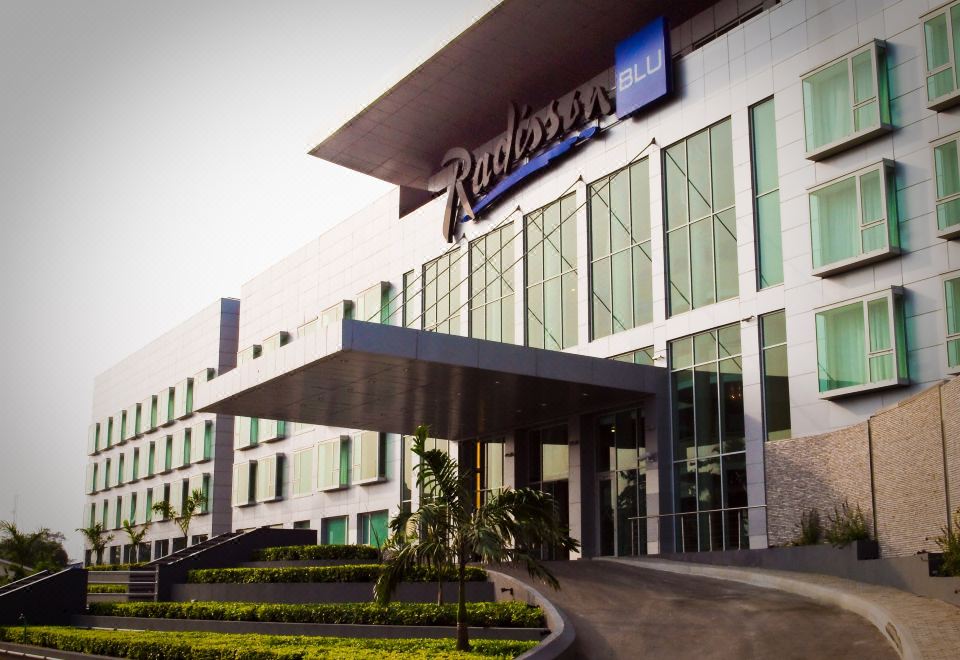 "a large hotel with a blue sign that reads "" radisson blu "" is surrounded by greenery" at Radisson Blu Anchorage Hotel
