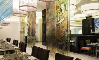 In the dining room, there are large tables and chairs, and along the wall, there is an artistic piece at Remis Hotel