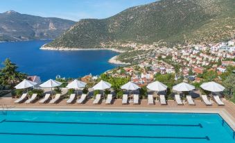 a beautiful resort with a swimming pool surrounded by lounge chairs and umbrellas , offering a view of the ocean and mountains at Happy Hotel Kalkan