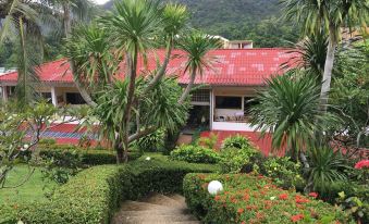 a house with a red roof is surrounded by palm trees and bushes , while a stone path leads to the entrance at Top Resort