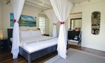 a large bed with white linens and a canopy is in a room with a wooden floor at Taveuni Palms Resort