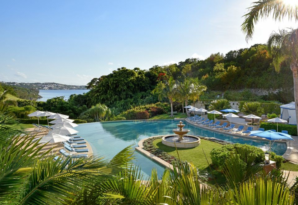 a large outdoor pool surrounded by lush green grass , with several lounge chairs and umbrellas placed around the pool area at Rosewood Bermuda