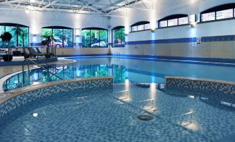 an indoor swimming pool with blue tiles and a white ceiling , surrounded by windows that allow natural light to enter the pool area at Village Hotel Manchester Hyde