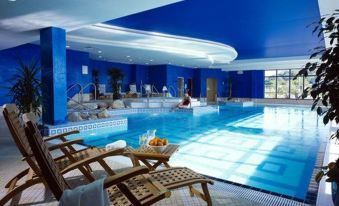 a large swimming pool with blue water and white tiles , surrounded by lounge chairs and a balcony at Actons Hotel Kinsale