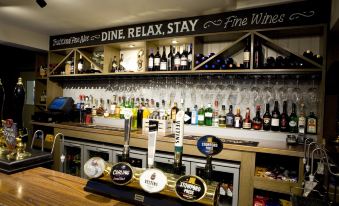 "a bar with a variety of beer taps and wine bottles , along with a sign that reads "" dine relax stay fine wines .""." at Burlton Inn