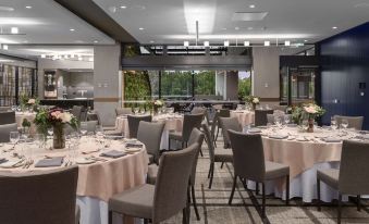 a well - lit restaurant with multiple dining tables set for guests , each table covered with white tablecloths and adorned with flowers at Rydges Campbelltown an EVT hotel