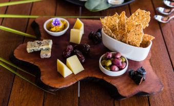 a wooden cutting board with various food items and snacks on it , including cheese , crackers , olives , and dried fruit at Kokomo Private Island Fiji