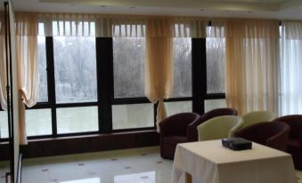 a living room with large windows and white curtains , featuring two brown chairs and a table in front at Alfa Hotel