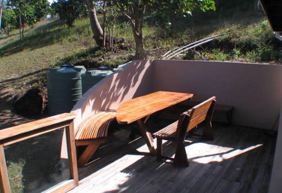 a wooden deck with a table and two chairs , surrounded by trees and a wall at Safari Lodge