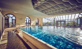 an indoor swimming pool with a large , blue water body and multiple people in the background at Hotel Nassauer Hof