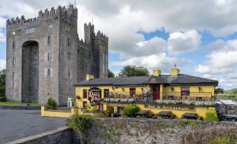 a castle - like building with a yellow exterior , situated next to a body of water and surrounded by trees at Bunratty Castle Hotel