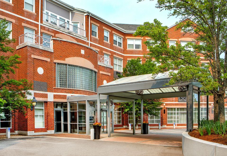 a brick building with an entrance and a covered walkway , surrounded by trees and people at Sheraton Portsmouth Harborside Hotel