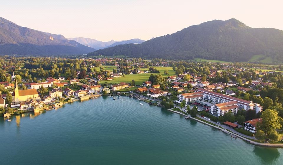 a bird 's eye view of a village nestled by the water with mountains in the background at Althoff Seehotel Uberfahrt
