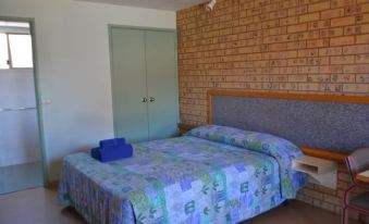 a bed with a blue and green floral blanket is in a room with brick walls at The Lodge Motel