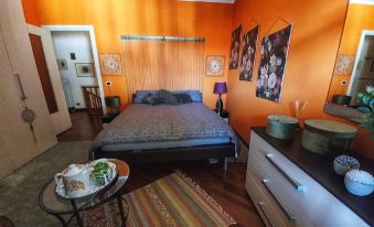 a cozy bedroom with an orange color scheme , featuring a bed , nightstand , and various items on the bedside table at CasAda