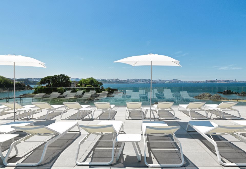 a large outdoor pool with white lounge chairs and umbrellas , surrounded by a beautiful view of the ocean at Noa Boutique Hotel