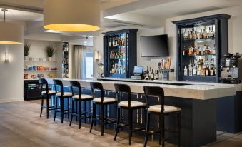 a well - lit bar area with a long wooden bar counter , several stools , and a television mounted on the wall at Delta Hotels Basking Ridge