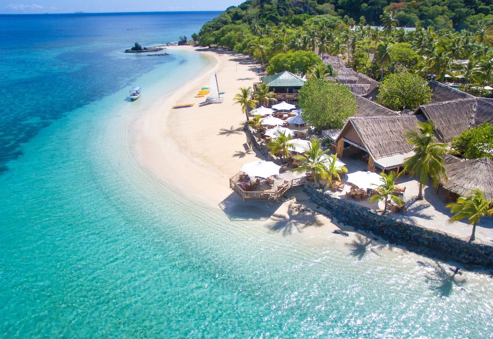 aerial view of a sandy beach with several palm trees and umbrellas , surrounded by blue water at Castaway Island Fiji
