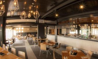 a modern restaurant with wooden tables and chairs , a bar area , and pendant lights hanging from the ceiling at Berri Hotel