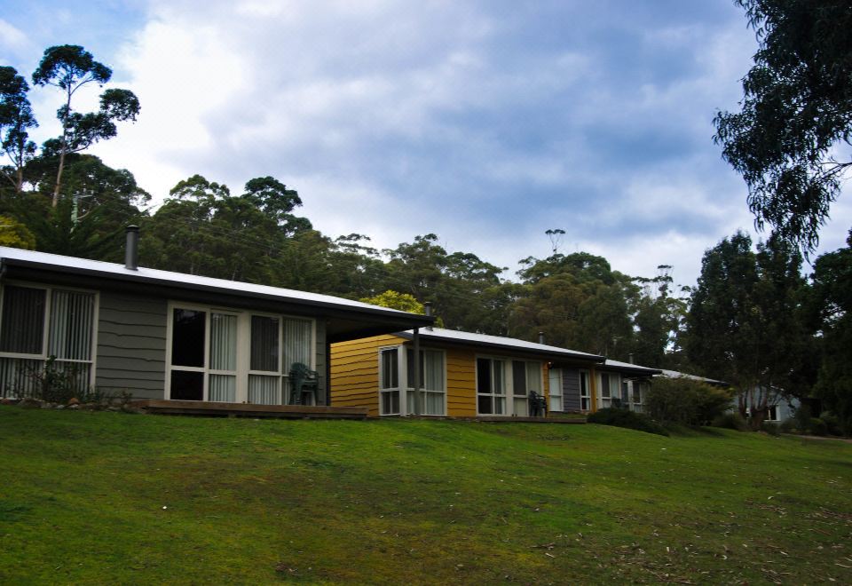 a group of small , yellow houses with white roofs are situated on a grassy hillside at Bruny Island Escapes and Hotel Bruny