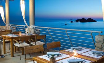 an outdoor dining area on a deck overlooking the ocean , with several chairs and tables set up for guests to enjoy their meals at Hotel Dubrovnik Palace