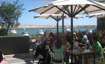 a group of people sitting outside at a restaurant under umbrellas , enjoying their time together at The Marina Hotel - Mindarie