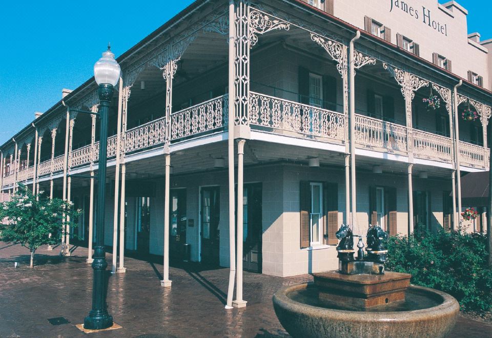 a large white building with multiple balconies and a fountain in front of it , surrounded by trees at St. James Hotel Selma, Tapestry Collection by Hilton