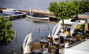 a group of people enjoying a meal at an outdoor restaurant by a body of water at Fletcher Hotel Restaurant Loosdrecht-Amsterdam
