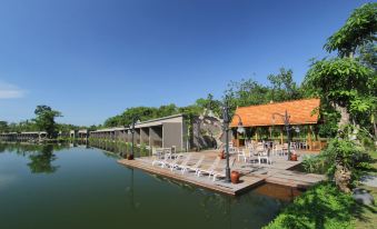 a serene lake with a wooden dock extending into the water , surrounded by trees and buildings at The Westlake Hotel & Resort Yogyakarta