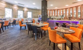 a modern dining room with orange chairs and tables , a bar area , and a black and purple bar at Bunbury Hotel Koombana Bay